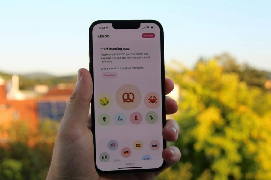 Uma mão segura um smartphone exibindo Melhores tradutores de voz e texto para viagens internacionais e um botão Download.